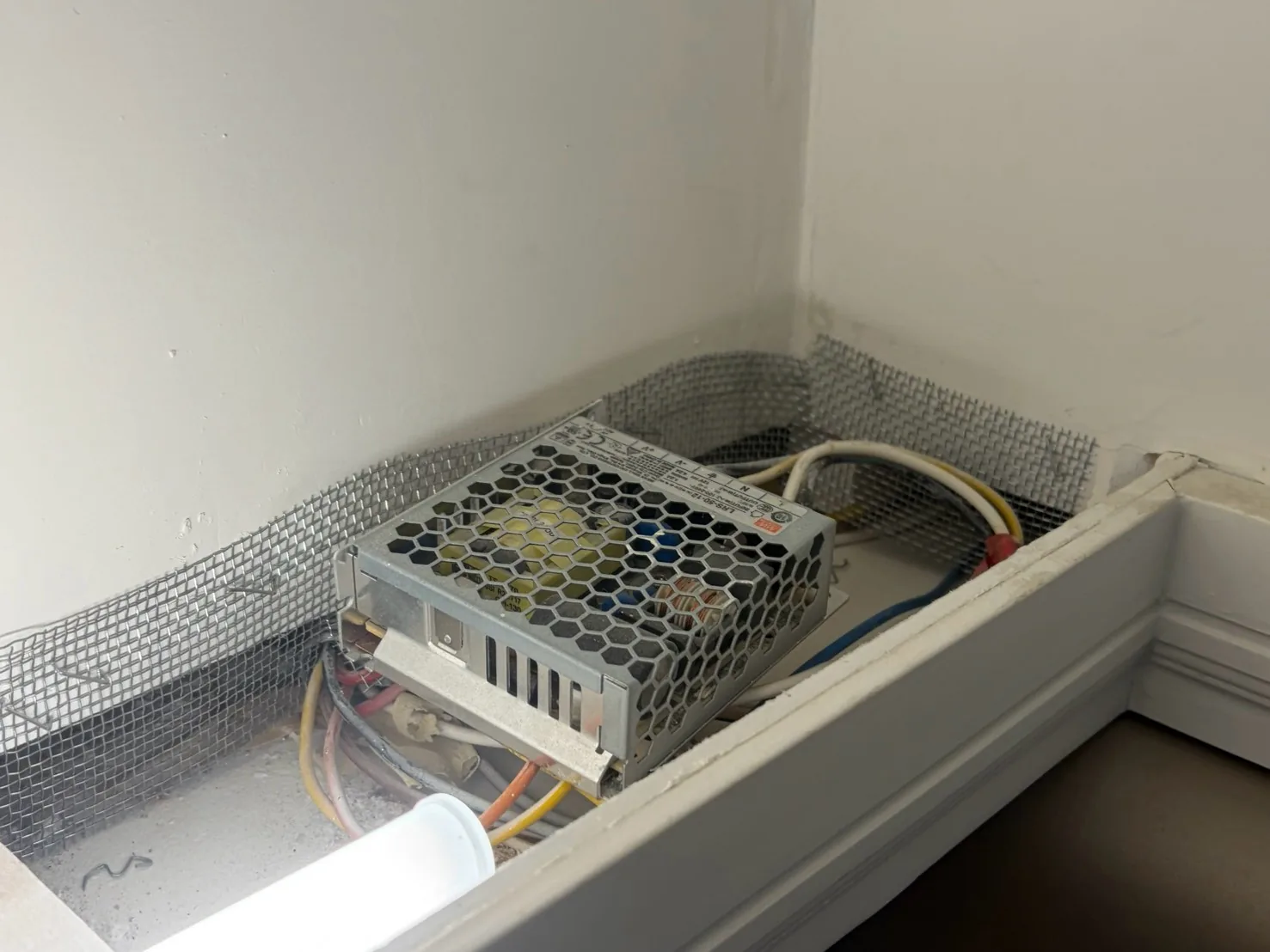 櫃體上方與牆面交接縫以不鏽鋼網條封邊，旁有燈具電源供應器