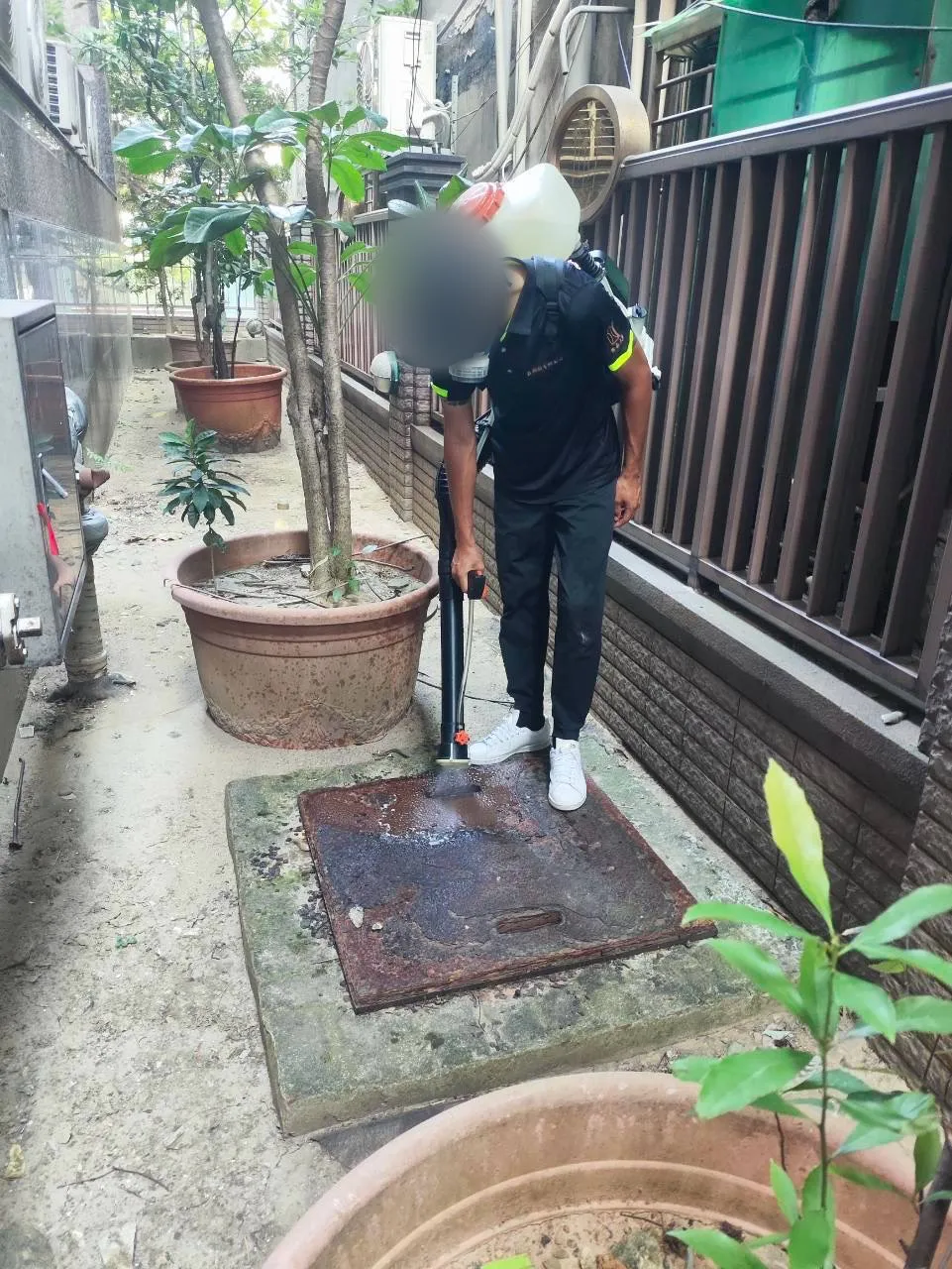 技師處理側庭地面孔蓋邊緣與接縫（臉部已模糊）