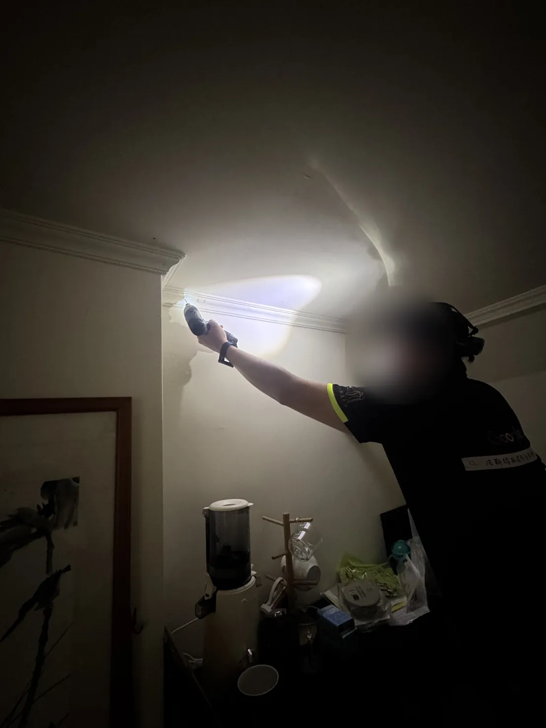 技師拿手電筒照天花板與牆面交界（臉部已模糊）