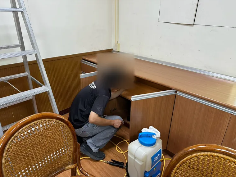 技師對茶水間下櫃內部施藥（臉部已模糊）