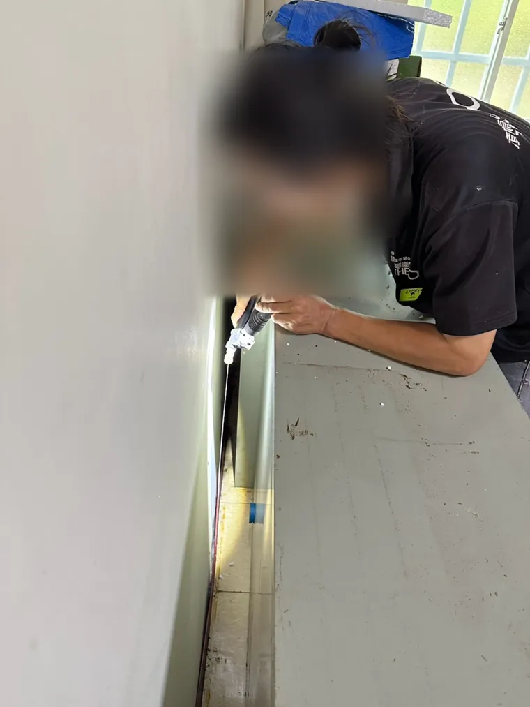 技師以手電筒照櫃子與牆之間的窄縫（臉部已模糊）