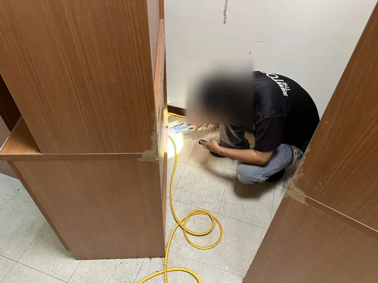 技師檢查兩個櫃子交接處的底部（臉部已模糊）