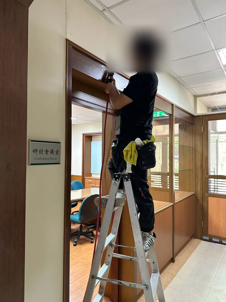 技師站梯子在會議室門框上緣鑽孔注藥（臉部已模糊）