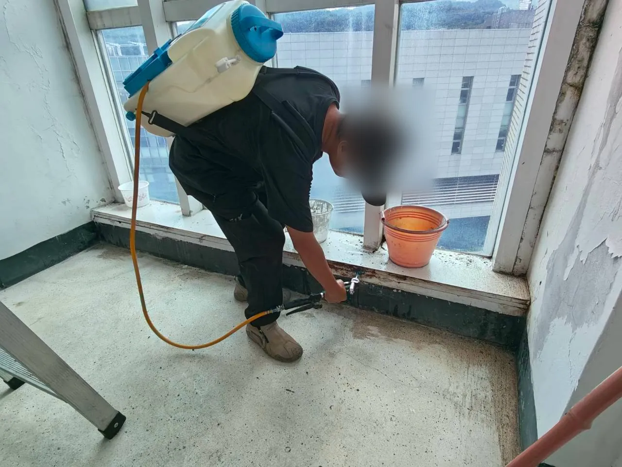 技師以電動背負噴霧器對窗台下緣與牆角接縫噴灑