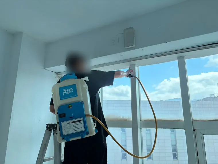 技師背電動噴霧器沿整排窗戶上緣噴灑