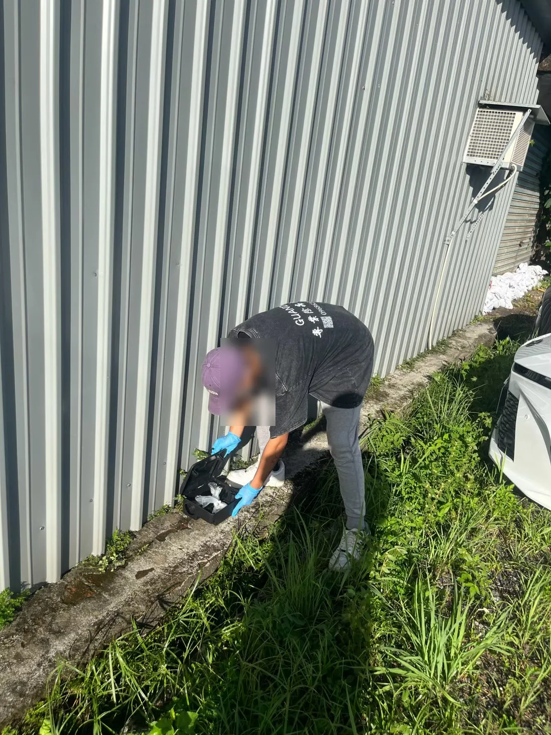 業者在鐵皮廠房外牆牆腳檢查鼠餌盒
