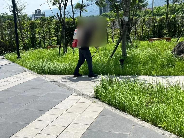 技師背電動噴霧器沿社區步道旁植栽根部噴灑