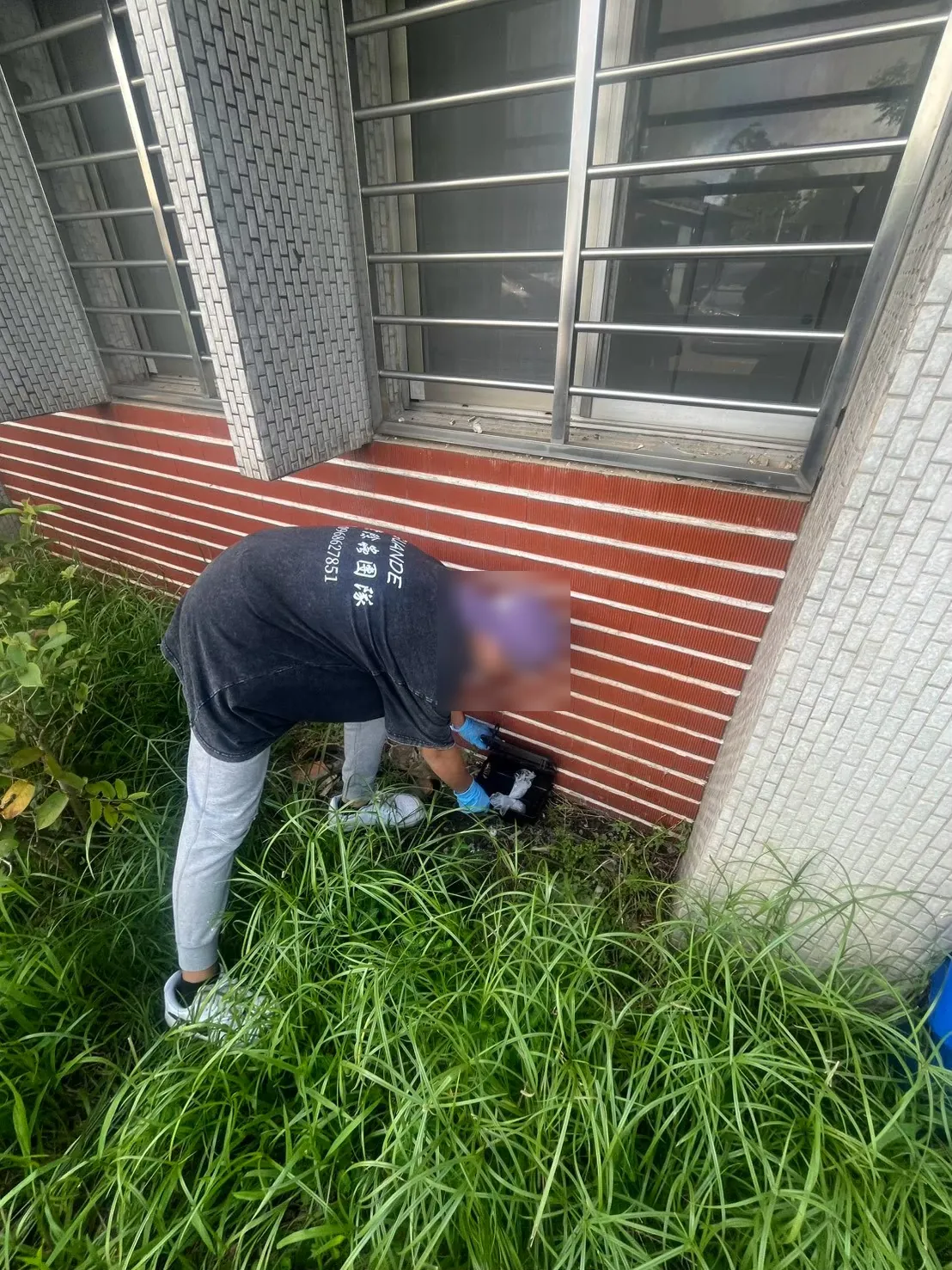 業者在店面外牆草叢邊打開鼠餌盒檢查